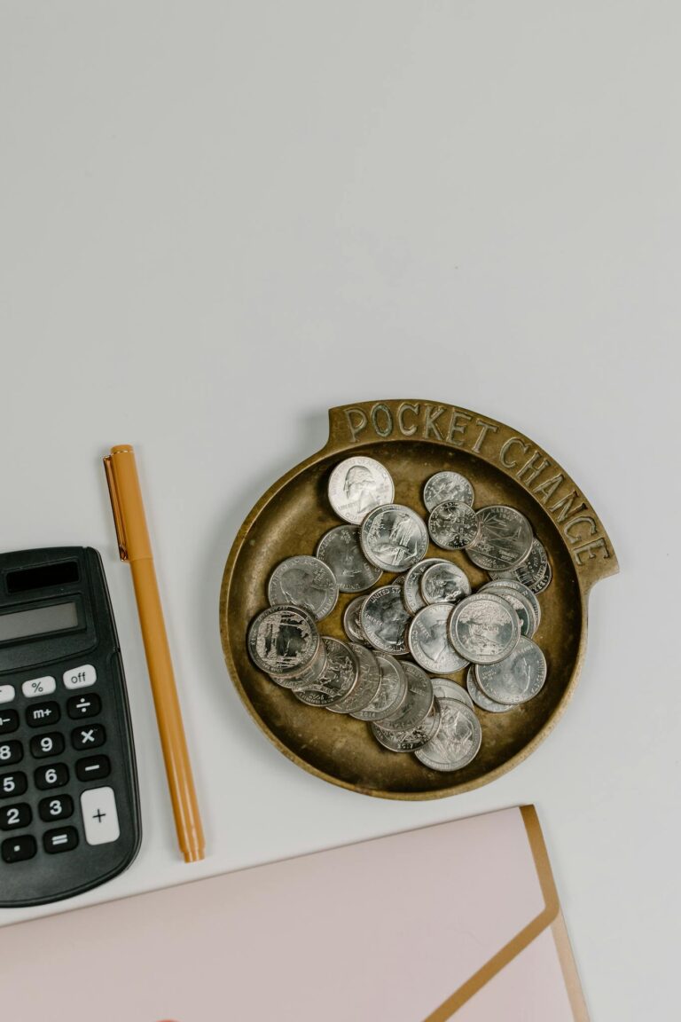 Top-down view of coins, calculator, and pen on a white surface, ideal for finance concept.